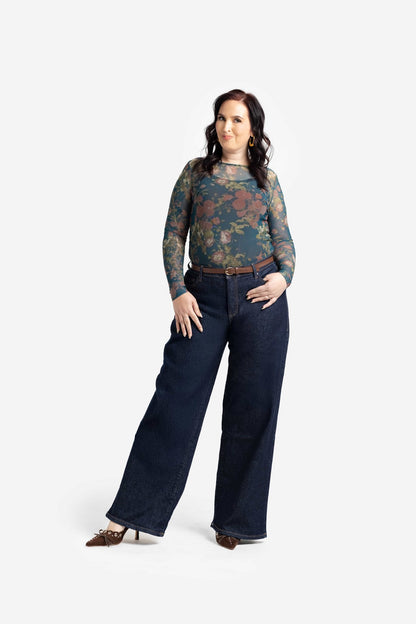 Woman wearing a patterned top and dark jeans on a white background