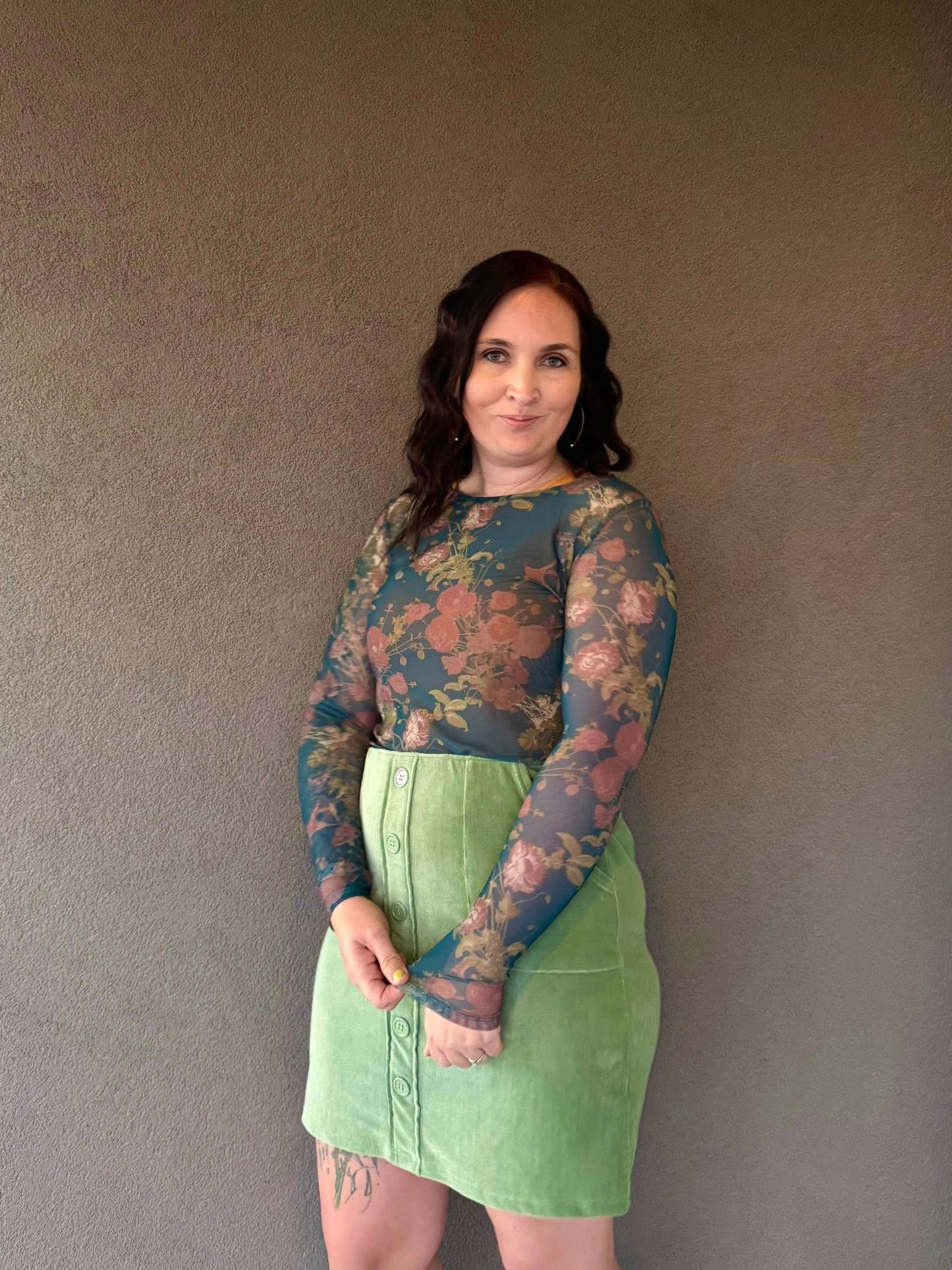 Woman wearing a floral long-sleeve top and green skirt against a plain background