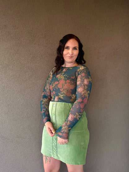 Woman wearing a floral long-sleeve top and green skirt against a plain background