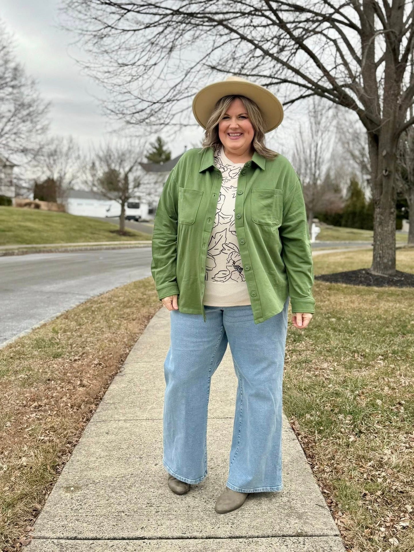 Model wearing the Myra Shacket in solid mossy olive green, a relaxed-fit French terry shirt jacket with button front and chest pockets, styled with wide-leg denim and a printed top outdoors on a sidewalk.