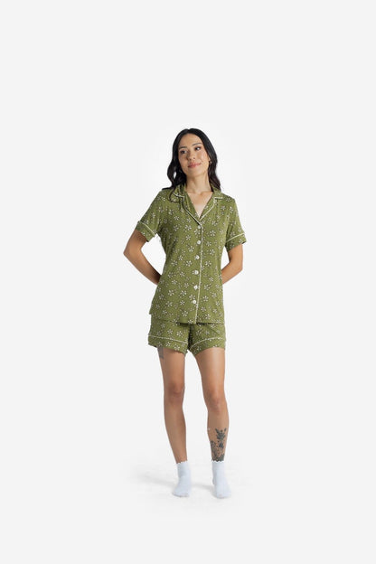 Woman wearing the LuLaRoe Candy PJ Set in an olive green ditsy floral print featuring small ivory flowers on an olive background with contrast piping, button-front pajama top, and matching pocket shorts on a white background
