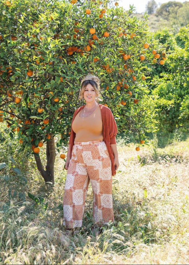 Woman standing in an orange grove with trees laden with oranges.