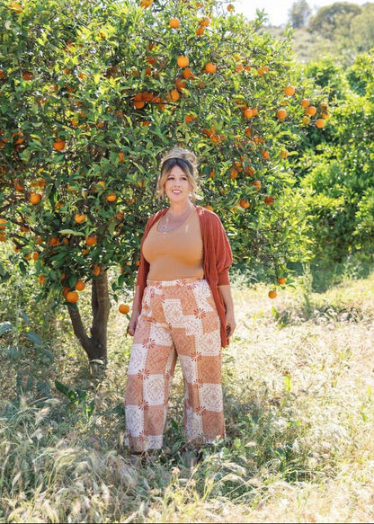 Woman standing in an orange grove with trees laden with oranges.