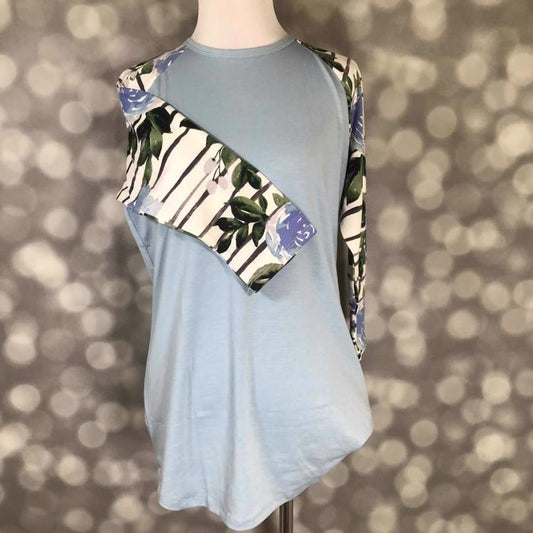LuLaRoe Randy Tee in dusty blue with floral striped sleeves featuring blue flowers and green leaves on a mannequin with a gray blurred background