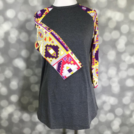 LuLaRoe Randy tee with charcoal gray body and purple yellow Aztec print raglan sleeves displayed on mannequin against a blurred background