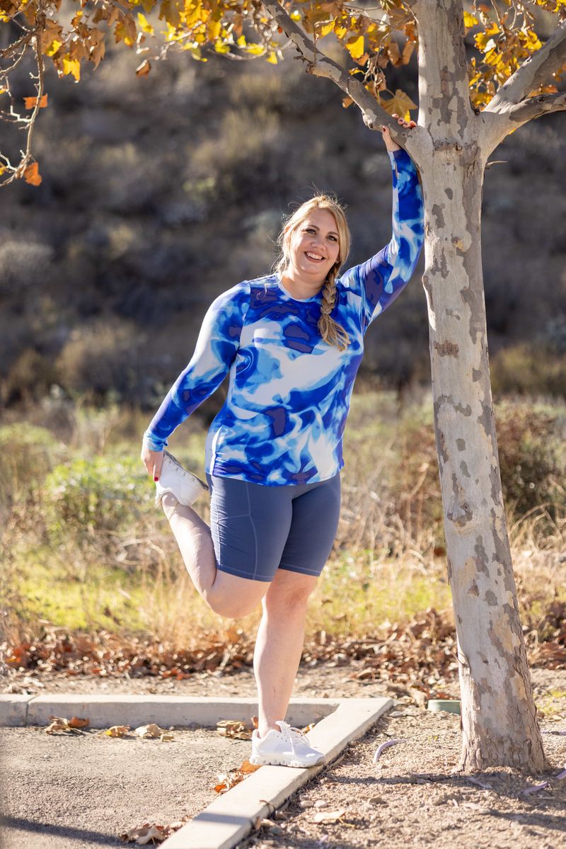 RISE Limitless Long Sleeve Top with a blue abstract pattern featuring light and medium blue tones, long sleeves, and a crew neckline worn by a model outdoors near a tree