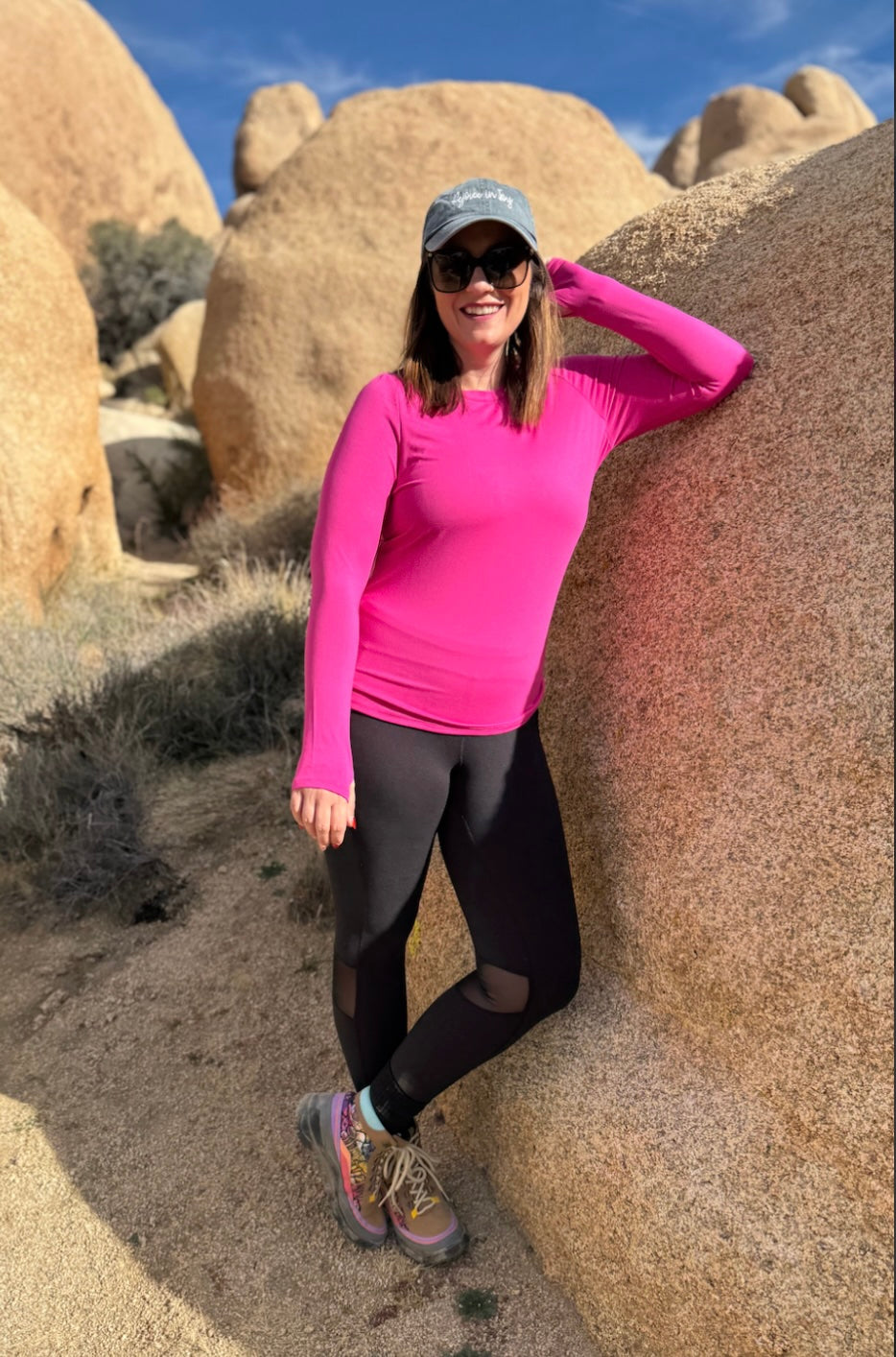 RISE Limitless Long Sleeve Top in vibrant fuchsia pink featuring long sleeves with thumb holes, a crew neckline, and smooth athletic jersey fabric, worn by a model standing in a desert landscape with large rocks.