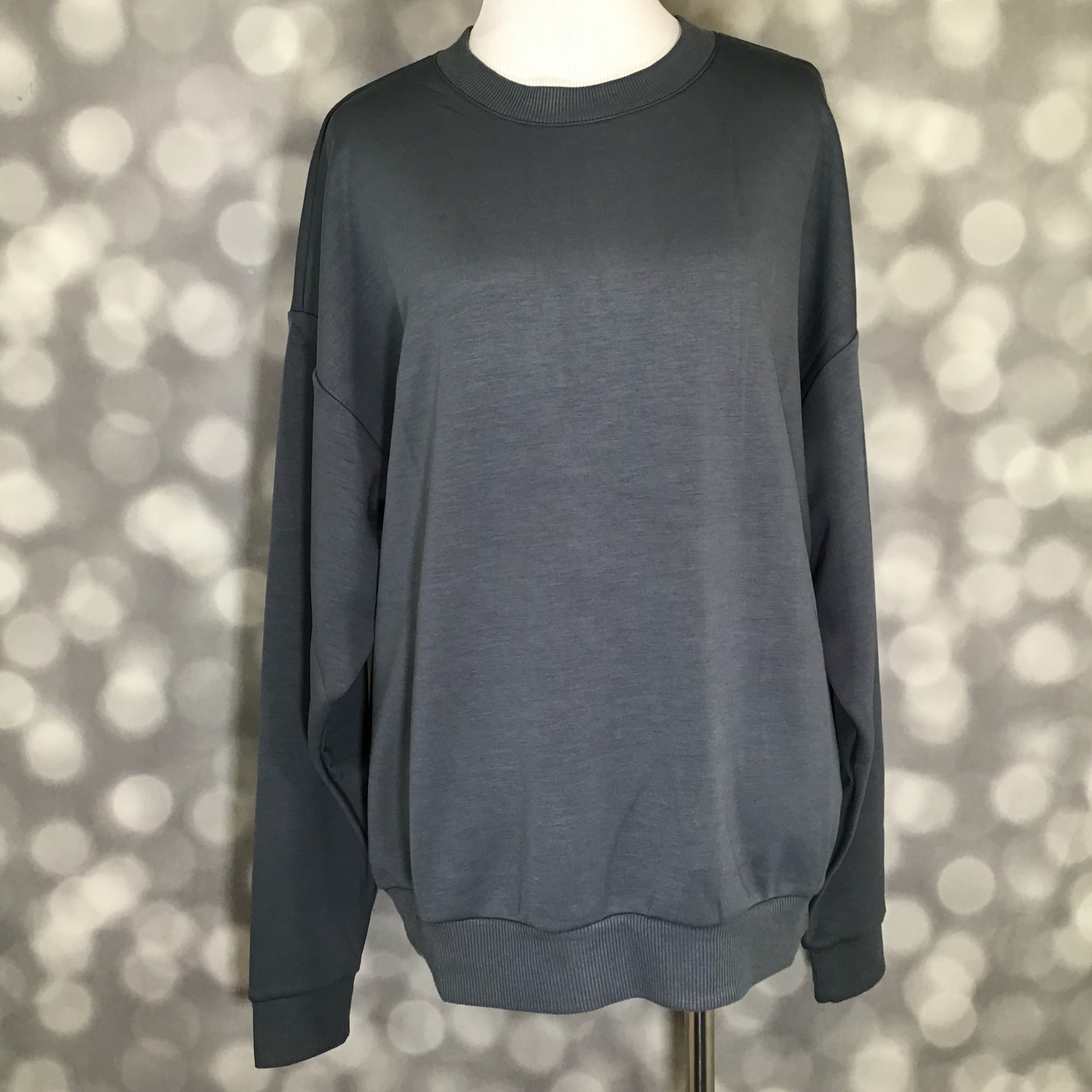 Rise Reset Crewneck Pullover in solid graphite gray with a relaxed oversized fit and ribbed hem on a mannequin against a bokeh background