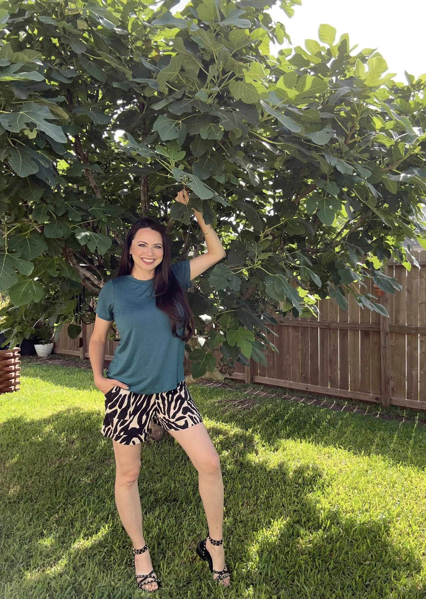 Woman wearing LuLaRoe Essential Tee in Solid Deep Teal featuring a rich blue-green color, classic crew neckline, short sleeves, and a semi-relaxed fit in soft luxe modal fabric in a garden with large green leaves in the background