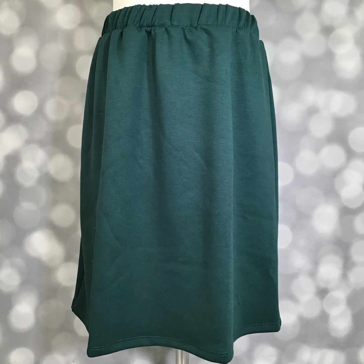 LuLaRoe Samantha Skirt in Solid Forest Pine, a women's pull-on midi skirt featuring a non-roll elastic waistband and soft Modal Scuba fabric. Rich forest green skirt with a flattering silhouette, perfect for everyday wear, office outfits, seasonal styling, and year-round comfort on a mannequin against a blurred background