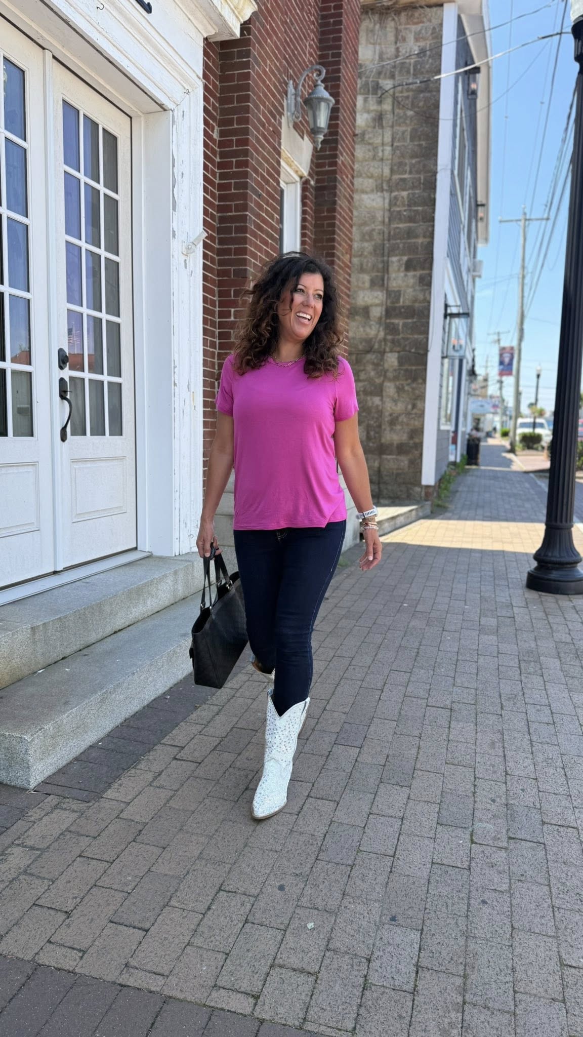 Woman wearing LuLaRoe Essential Tee in Solid Fuchsia Bloom featuring a vibrant pink color, classic crew neckline, short sleeves, and a semi-relaxed fit in soft luxe modal fabric and white boots walking on a sidewalk.
