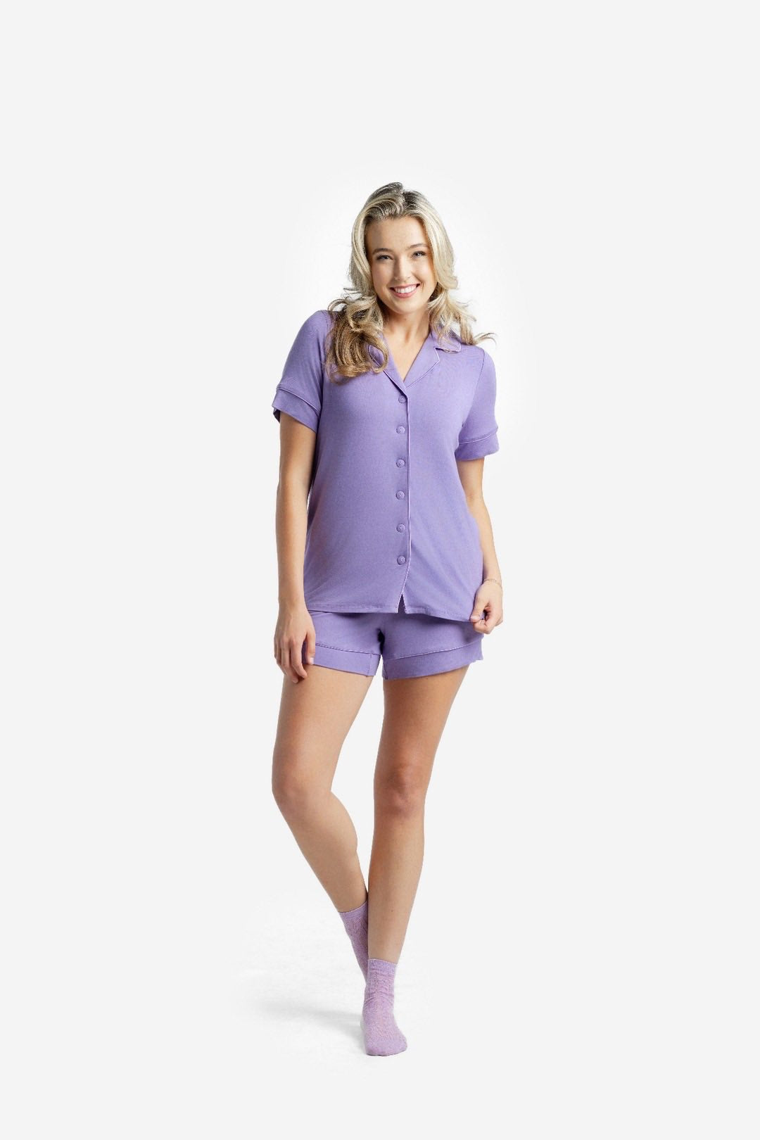 Woman wearing the LuLaRoe Candy PJ Set in Solid Lavender Mist featuring a button-front short sleeve pajama top and matching relaxed-fit pocket shorts in a soft lavender purple color on a white background