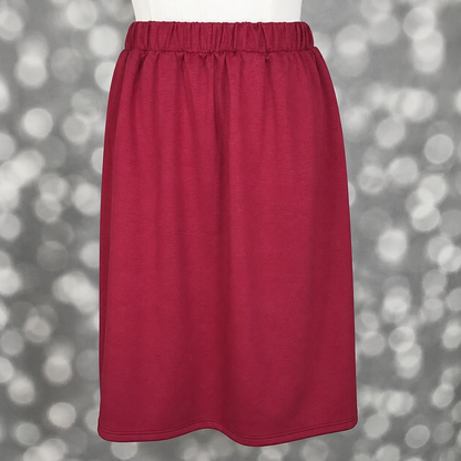 LuLaRoe Samantha Skirt in Solid Raspberry Wine, a women's pull-on midi skirt featuring a comfortable non-roll elastic waistband and soft Modal Scuba fabric. Rich raspberry red skirt with a flattering silhouette for everyday wear, work outfits, and seasonal styling on a mannequin against a blurred gray background