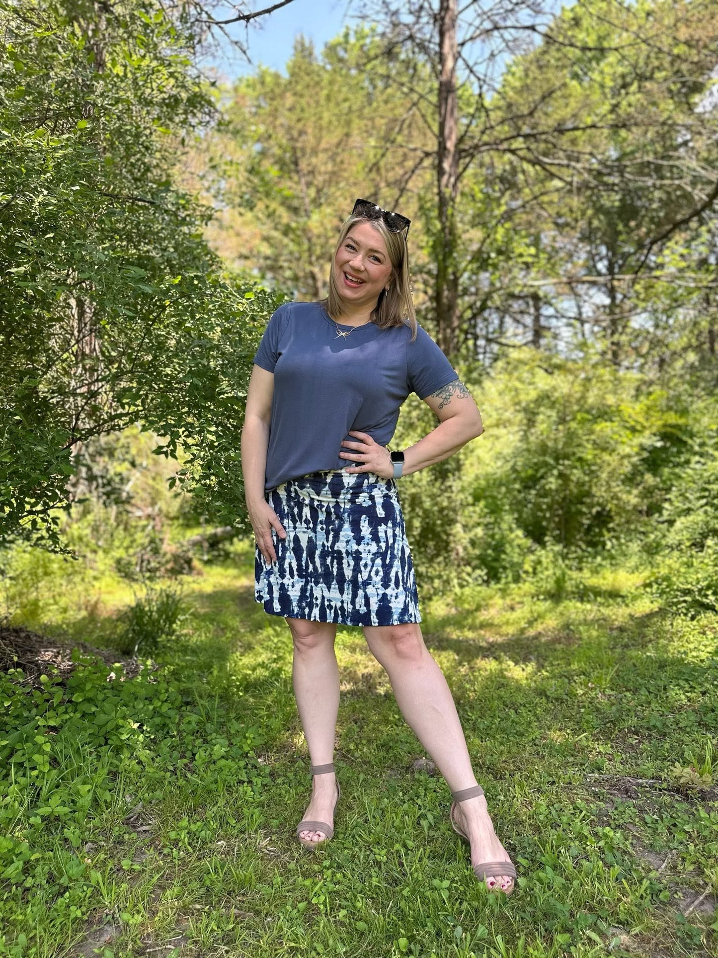 Woman standing in a forest wearing LuLaRoe Essential Tee in Solid Stormy Blue featuring a muted blue-gray color, classic crew neckline, short sleeves, and a semi-relaxed fit in soft luxe modal fabric.