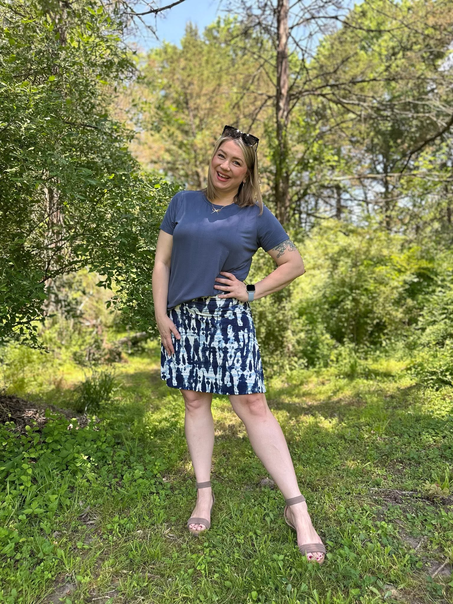 Woman standing in a forest wearing LuLaRoe Essential Tee in Solid Stormy Blue featuring a muted blue-gray color, classic crew neckline, short sleeves, and a semi-relaxed fit in soft luxe modal fabric.