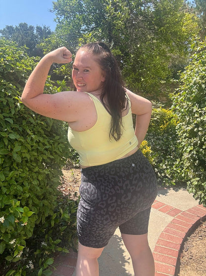 Person flexing arm muscles outdoors wearing a solid Citrus Glow LuLaRoe Resilient Cami bralette with greenery in the background