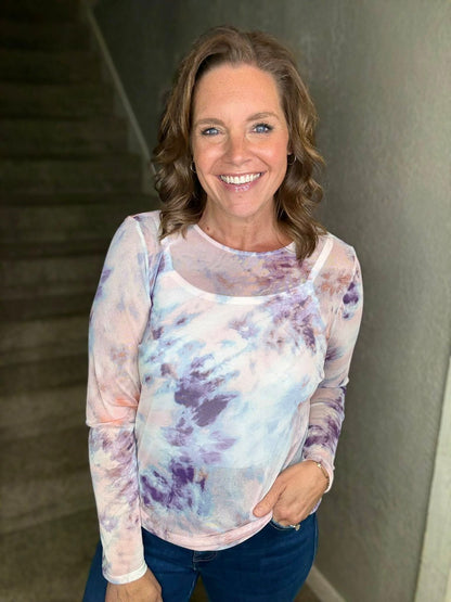 Woman wearing a tie-dye shirt standing against a neutral wall.